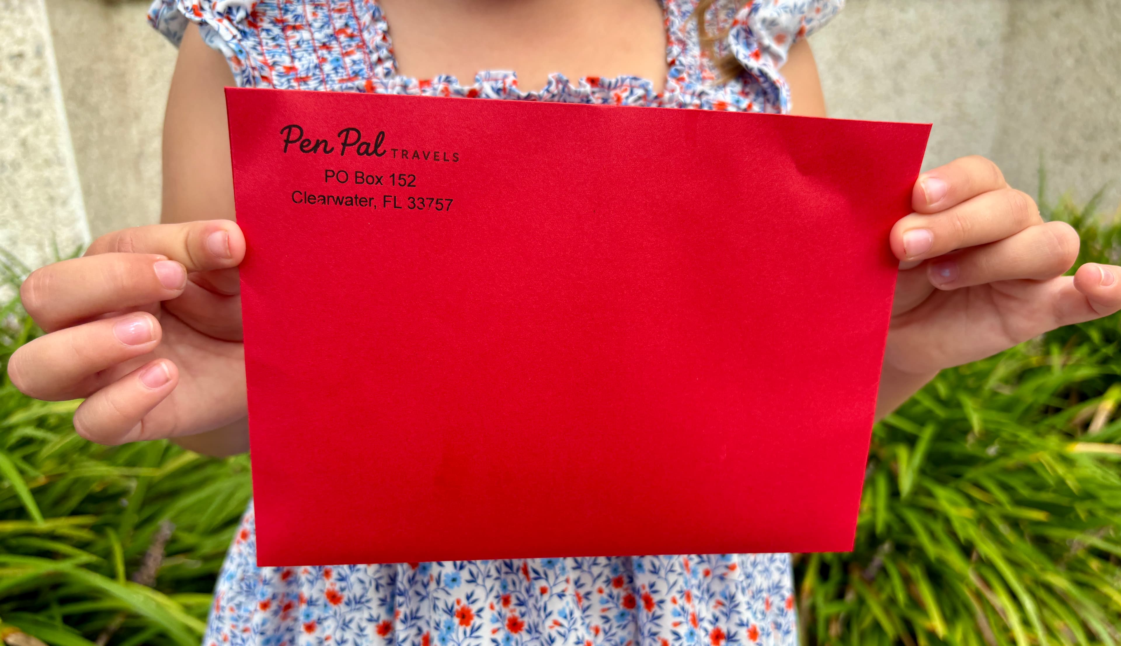 Child holding a bright red Pen Pal Travels envelope